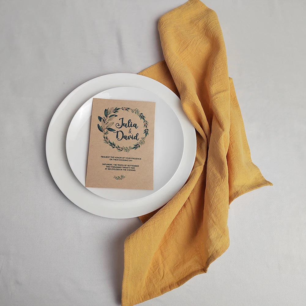 L'image présente un carton d'invitation de mariage entre Julia et David, posé sur une assiette blanche avec une serviette en tissu jaune à côté.