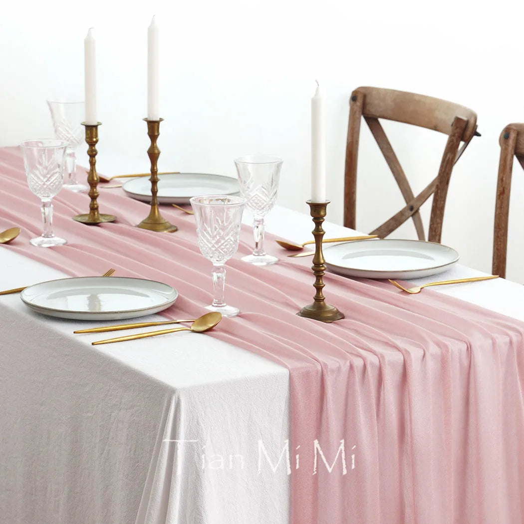 Une table élégante décorée de bougies, de verres et d'ustensiles de service en or, sur une nappe rose délicate.