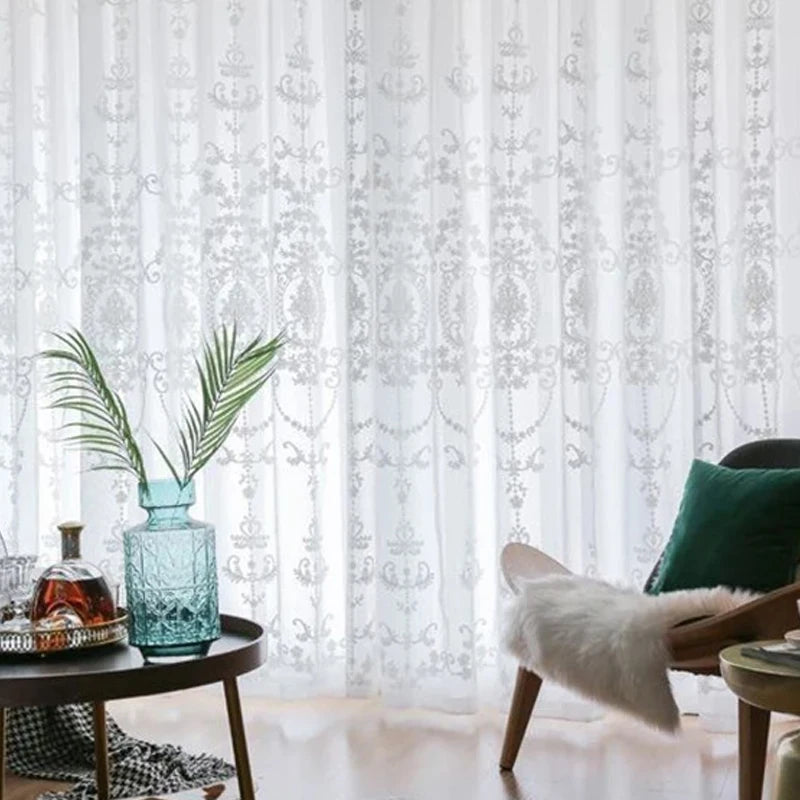 Décoration intérieure avec voilage blanc brodé, table basse noire et chaise design avec coussin vert.