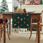 La table est agrémentée d'un chemin de table aux motifs de Noël, avec des boules, des cadeaux et des silhouettes de Père Noël, créant une ambiance festive et chaleureuse.