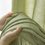 Zoom sur la texture épaisse et naturelle du rideau vert amande tenu dans une main.