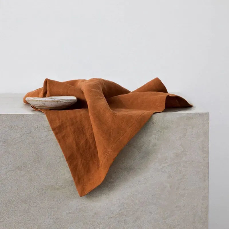 Couverture en laine marron enroulée autour d'un bol blanc posé sur un socle en béton gris.