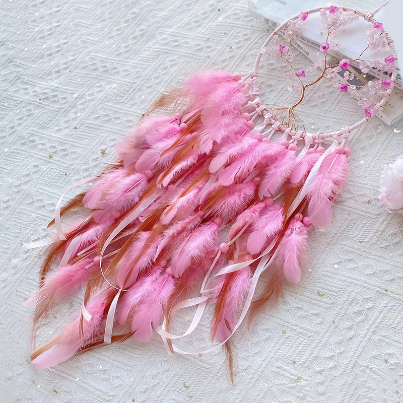 Un attrape-rêves rose orné de plumes et de cristaux, suspendu sur un fond blanc texturé.