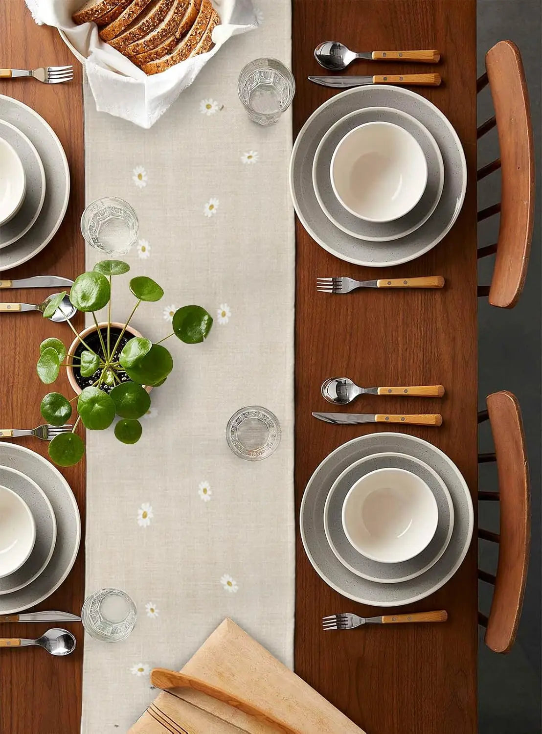 Une table à manger élégante avec une belle vaisselle grise, des couverts en bois et une plante verte au centre, décorée avec de jolies fleurs blanches.