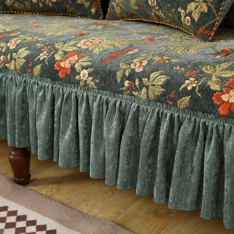 Lit meublé d'une grande couvre-lit ornée de motifs floraux multicolores dans des tons verts, avec une bordure froncée assortie.