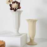 Deux vases en céramique blanche et crème avec des fleurs ornementales brunes et blanches posées sur un présentoir blanc.