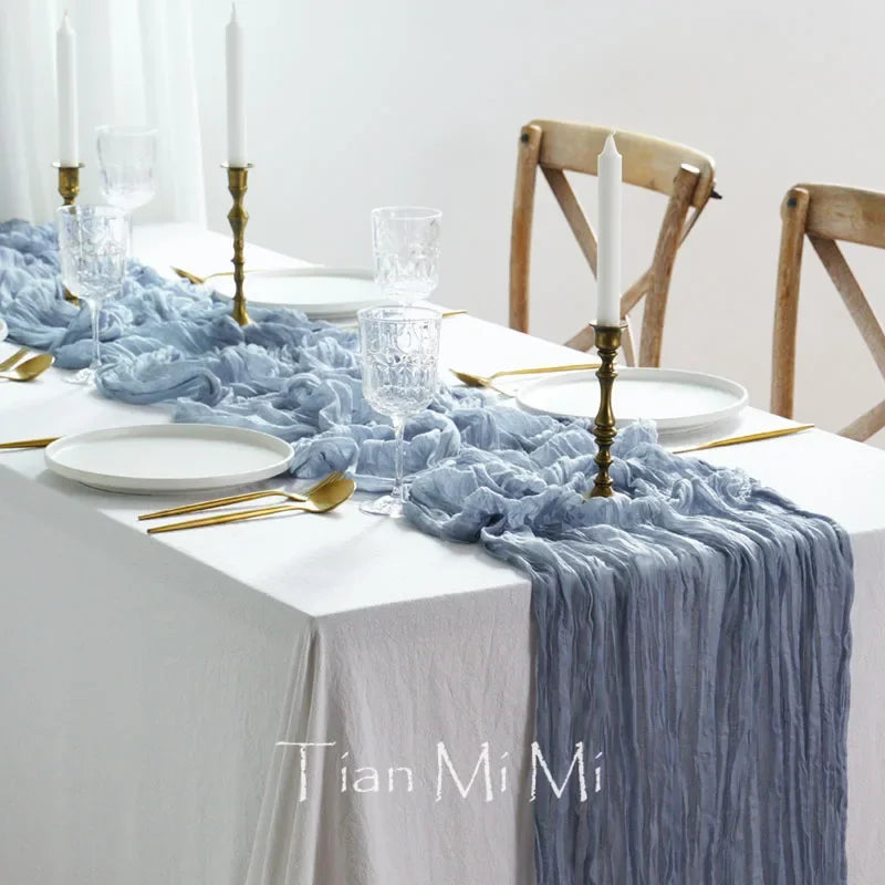 Une table élégante avec une nappe blanche et une décoration bleu ciel, avec des chandelles, des couverts dorés et des verres en cristal, créant une ambiance raffinée et chaleureuse.