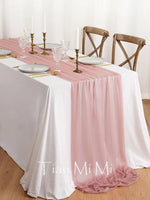 Une table élégante avec de la vaisselle, des bougeoirs dorés et une nappe blanche et rose, créant une ambiance chaleureuse et raffinée.