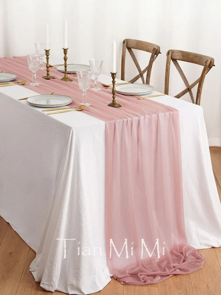 Une table élégante avec de la vaisselle, des bougeoirs dorés et une nappe blanche et rose, créant une ambiance chaleureuse et raffinée.
