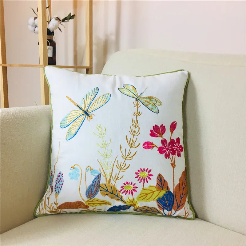 Cette image représente un coussin décoratif orné de motifs floraux et d'insectes, tels que des libellules, dans des couleurs vives et joyeuses, créant une atmosphère chaleureuse et naturelle dans l'espace.