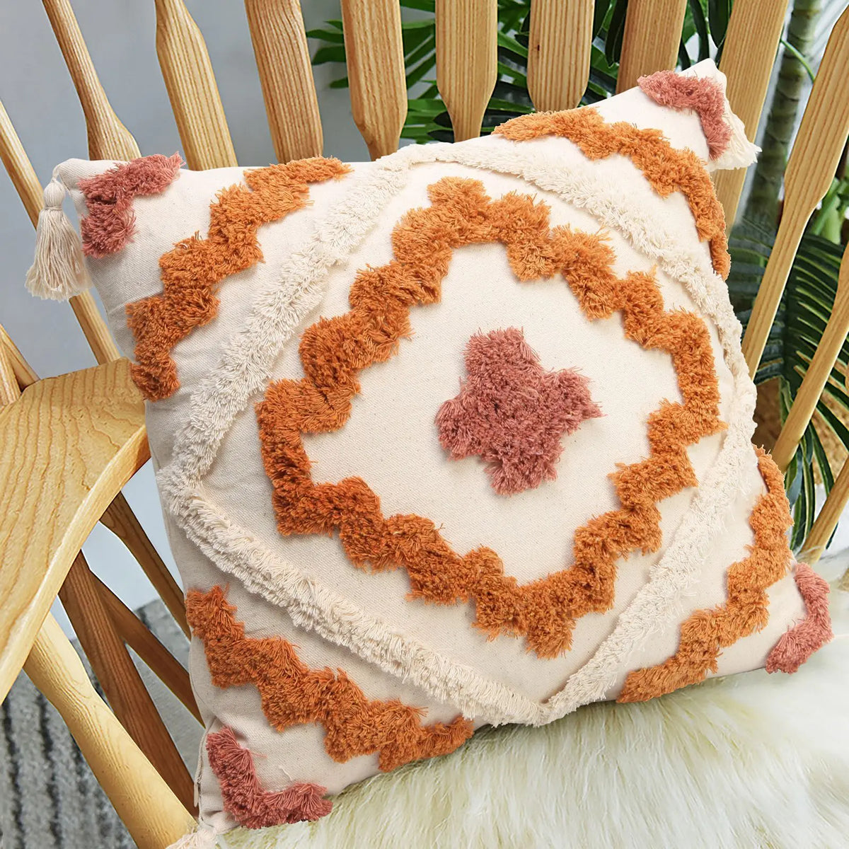 Coussin en tissu à motifs géométriques chauds, avec des franges et des motifs en relief, décorant une chaise en bois au milieu d'un décor végétal.