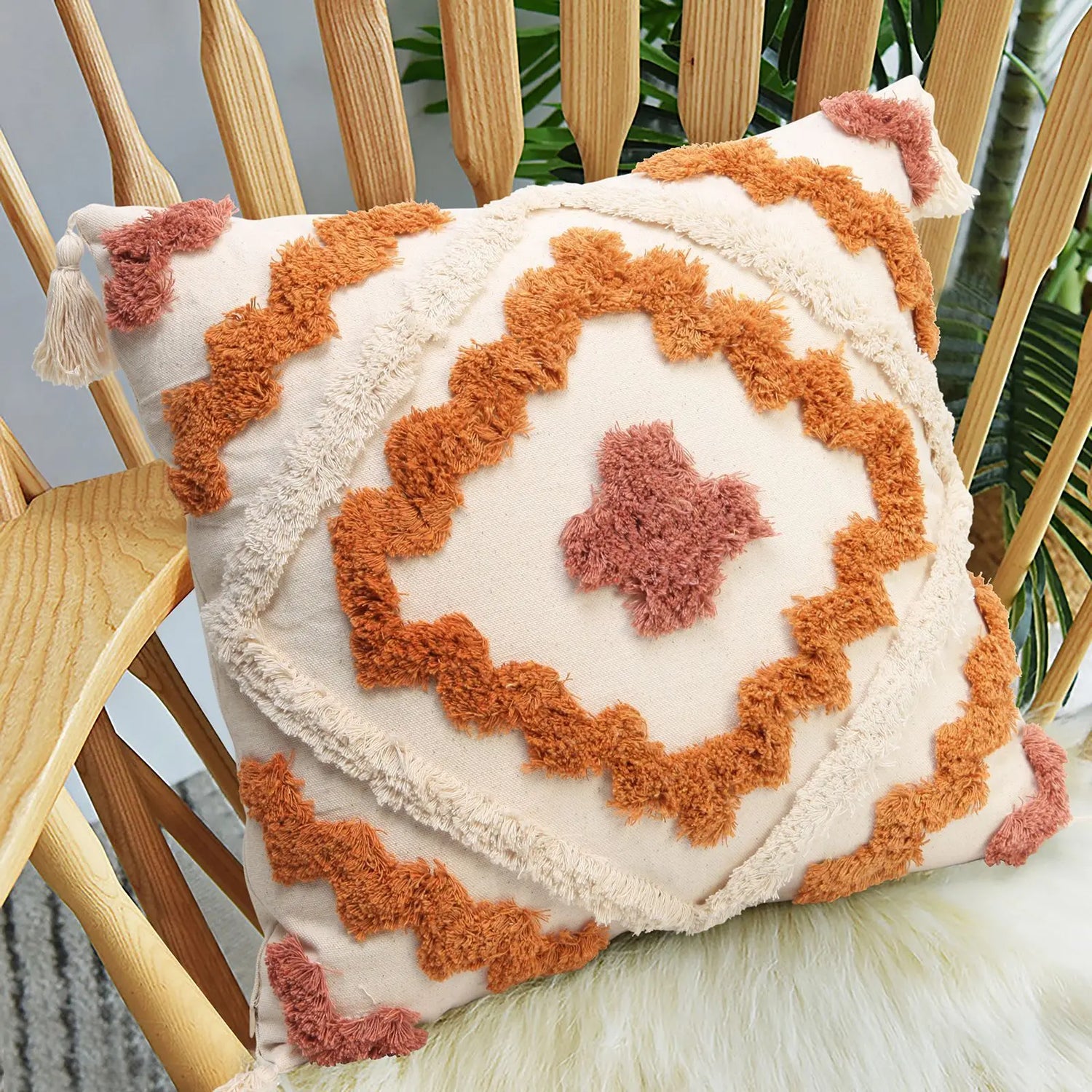 Coussin en tissu à motifs géométriques chauds, avec des franges et des motifs en relief, décorant une chaise en bois au milieu d'un décor végétal.