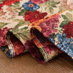 Motif floral coloré et vivace sur textile, avec des fleurs rouges, bleues et vertes délicatement tissées sur un fond beige.