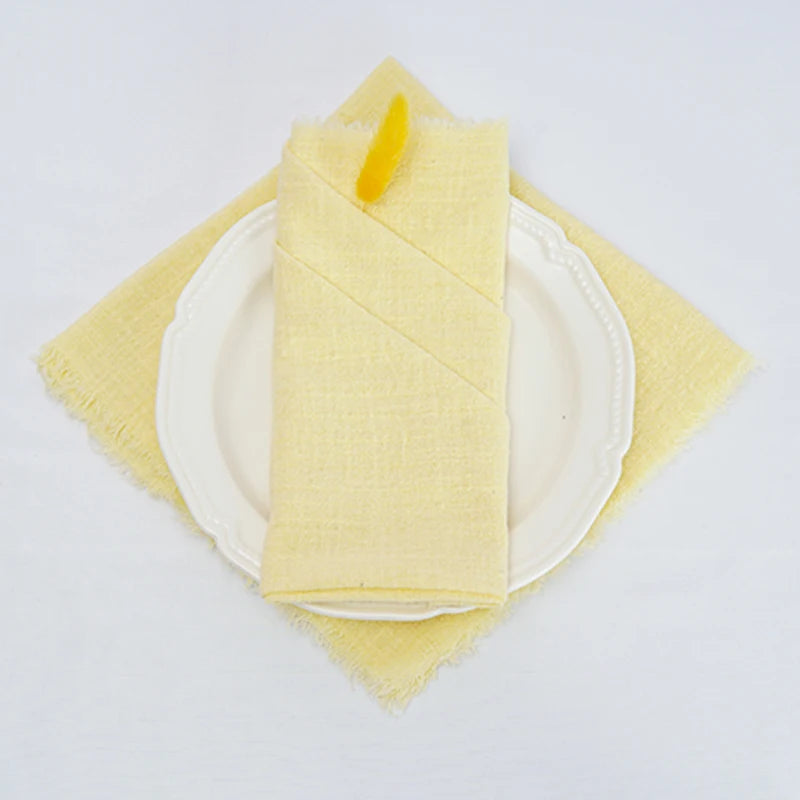 Une serviette de table en coton jaune pâle soigneusement pliée sur une assiette blanche.