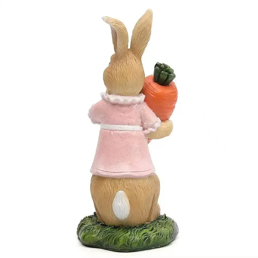 Une statuette décorative en forme de lapin mignon, portant un vêtement rose pâle et tenant une carotte orange.