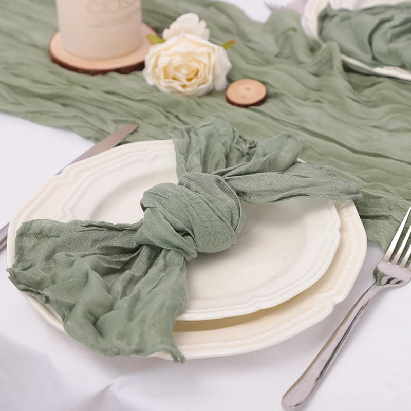 Une nappe de table en tissu vert pastel et des assiettes de service posées sur une surface blanche, avec des détails décoratifs comme une rose blanche et des petits disques en bois.