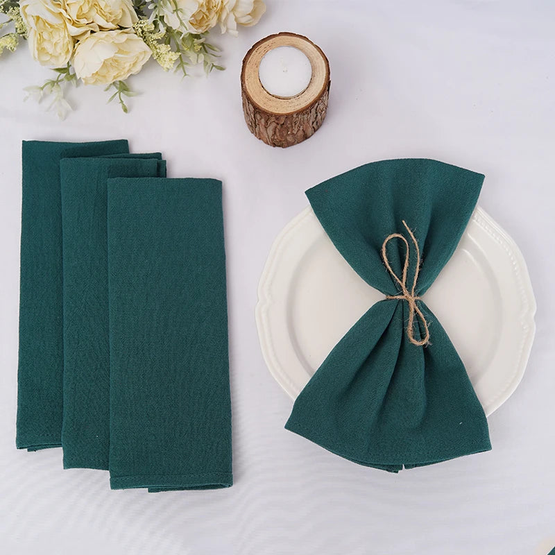 Arrangement de serviettes de table en tissu vert foncé, assiette blanche, bougeoir en bois sur fond blanc avec des fleurs blanches.