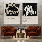 Deux affiches minimalistes en noir et blanc encadrent deux fauteuils en velours marron, créant une ambiance contemporaine et élégante.