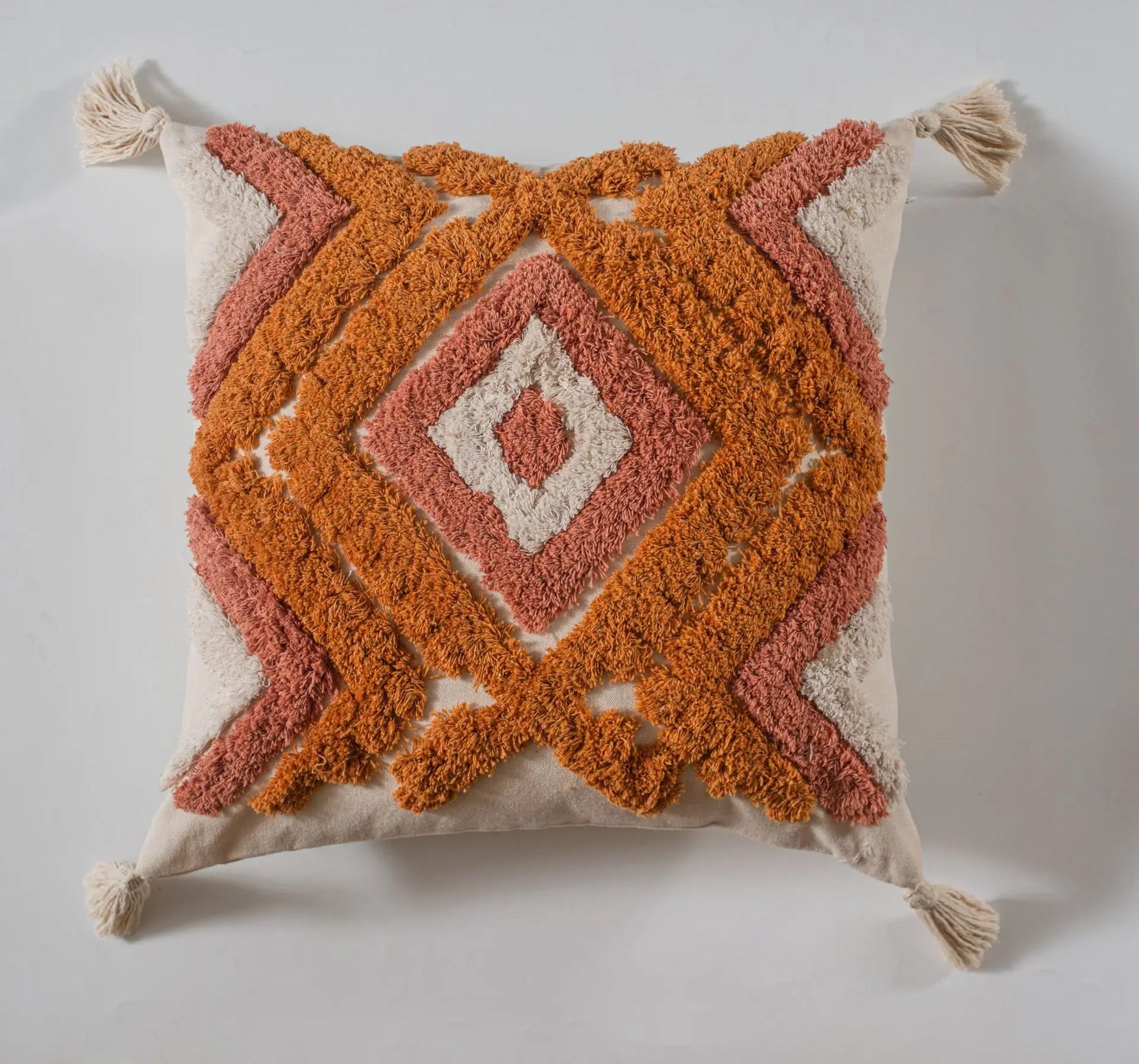 Coussin décoratif avec un motif géométrique en tons oranges et roses sur un fond beige.