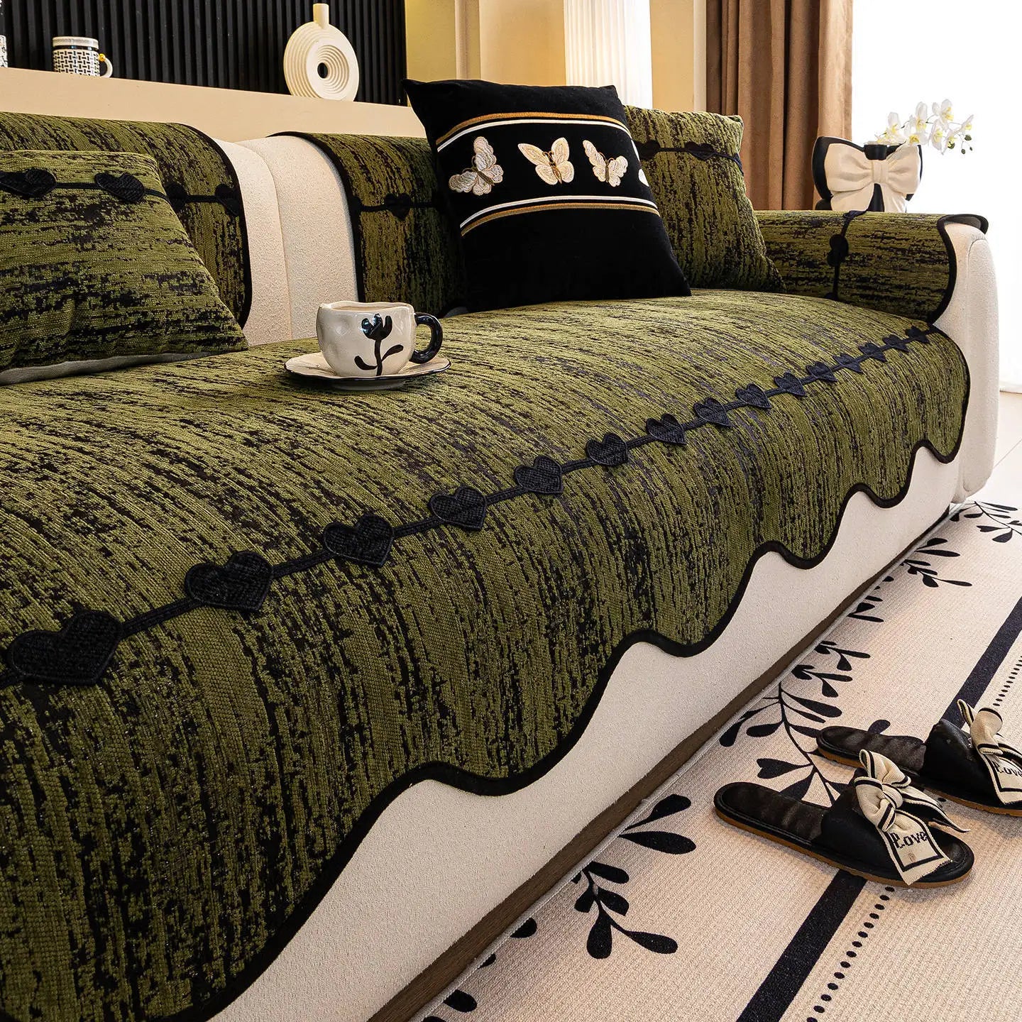 Un grand lit aux couleurs olive et noires avec des motifs de papillons et de feuilles, un bol de céramique décoré et un ruban noir noué formant un décor élégant et raffiné.