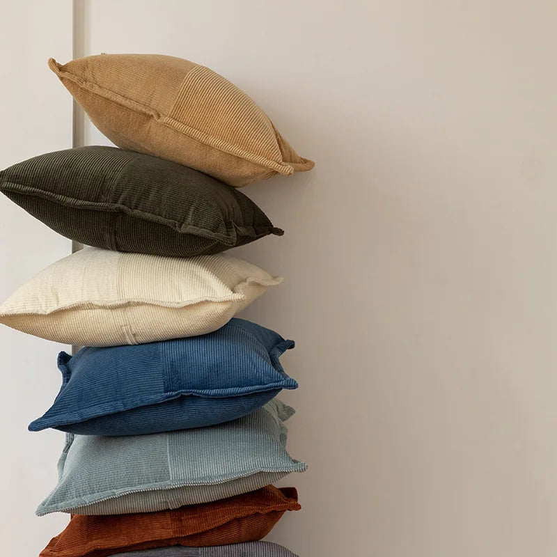 Pile de coussins de différentes couleurs et textures sur un mur clair, créant une ambiance douce et apaisante.