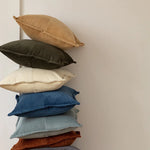 Pile de coussins de différentes couleurs et textures sur un mur clair, créant une ambiance douce et apaisante.