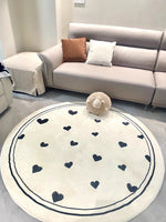 Un tapis rond blanc avec des motifs de coeurs noirs décore un salon cosy avec un canapé gris et des oreillers décoratifs.