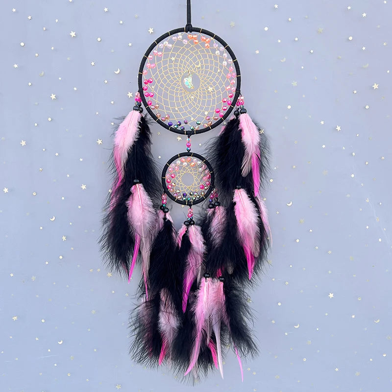 Un capteur de rêves décoratif, composé de cercles noirs et roses ornés de plumes, suspendu dans un ciel étoilé.