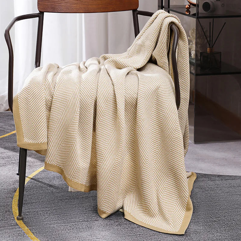 Une élégante couverture tricotée de couleur beige et crème, douillette et confortable, reposant sur un fauteuil dans un intérieur moderne.
