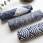 Des rouleaux de tissu avec des motifs géométriques bleus et blancs, enroulés et attachés avec de la ficelle.