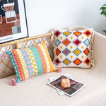 Coussins colorés aux motifs géométriques sur un fauteuil en osier avec une affiche murale abstraite.