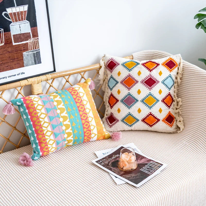 Coussins colorés aux motifs géométriques sur un fauteuil en osier avec une affiche murale abstraite.