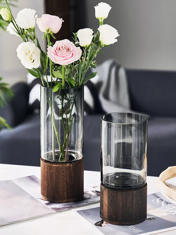 Un magnifique bouquet de roses roses et de fleurs blanches, délicatement disposées dans un vase en verre posé sur un support en bois, créant une scène élégante et raffinée.