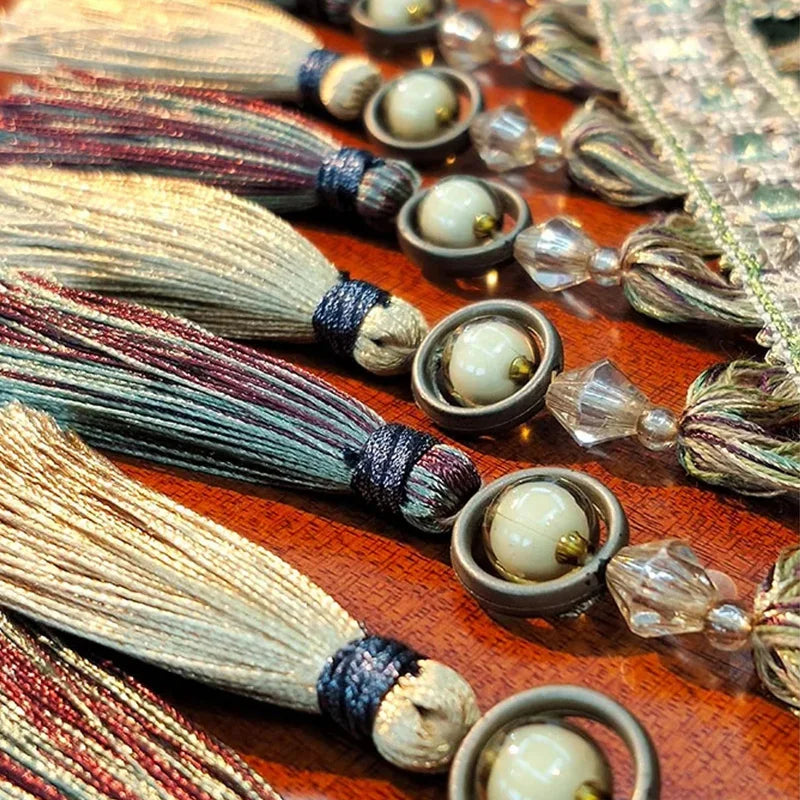 L'image montre des glands colorés et des perles ornementales sur un fond texturé, formant un motif décoratif élégant.