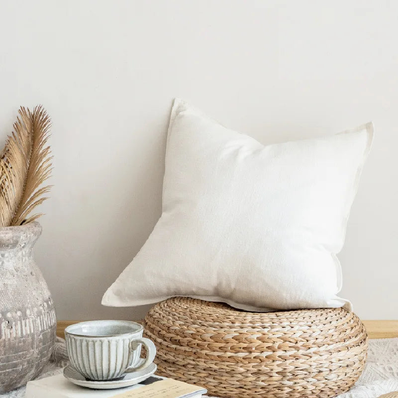 Coussin blanc confortable posé sur un panier en tressage naturel, accompagné d'une tasse de thé et d'un vase décoratif, dans un intérieur épuré et lumineux.