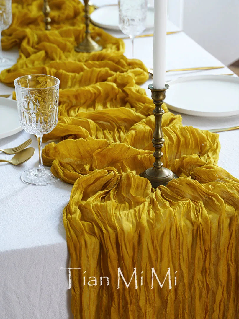 L'image présente une table de salle à manger élégante avec une nappe en tissu froissé de couleur jaune vif, un chandelier ancien et des verres de cristal, donnant une ambiance chaleureuse et raffinée.