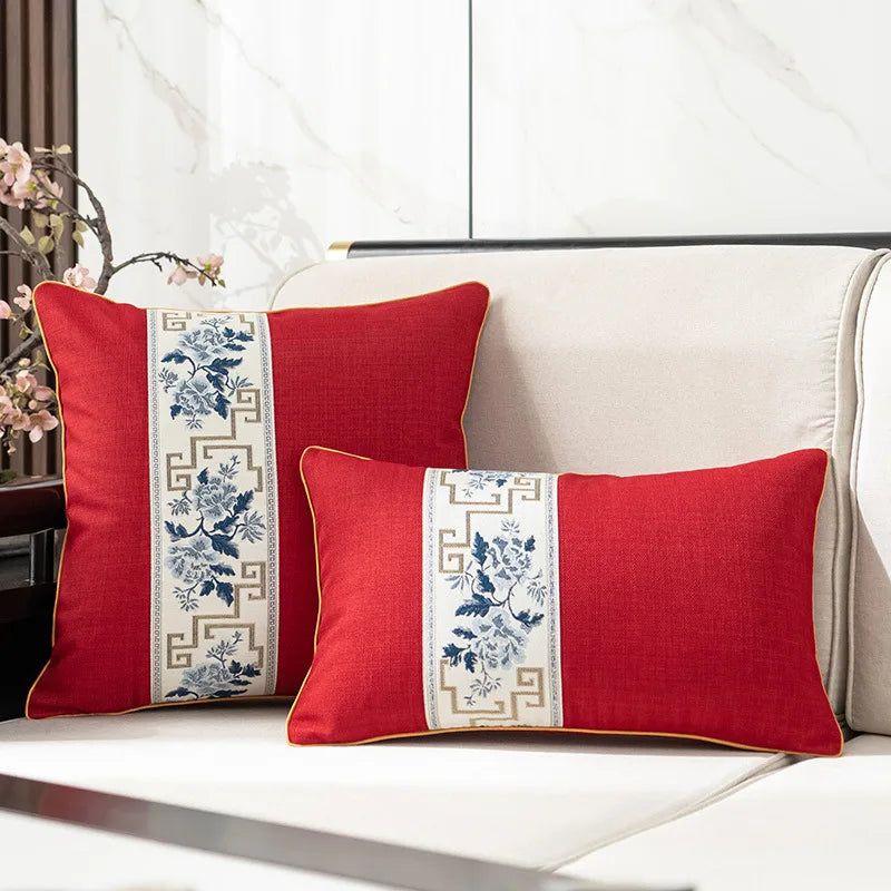 Deux coussins décoratifs rouges avec des motifs floraux bleus et beiges, placés sur un canapé beige.