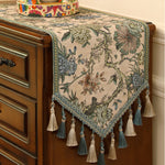 Magnifique chemin de table fleuri avec des motifs colorés et ornements de glands en tissu décorant avec élégance le meuble en bois.