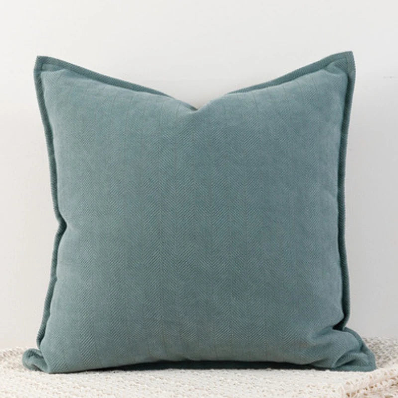 Oreiller décoratif en tissu gris-vert avec un motif de chevrons, posé sur une surface neutre.