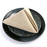 Serviette beige pliée sur un plat en céramique noir avec un motif texturé.