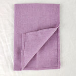 Couverture tricotée en laine de couleur lilas, pliée sur un fond blanc.