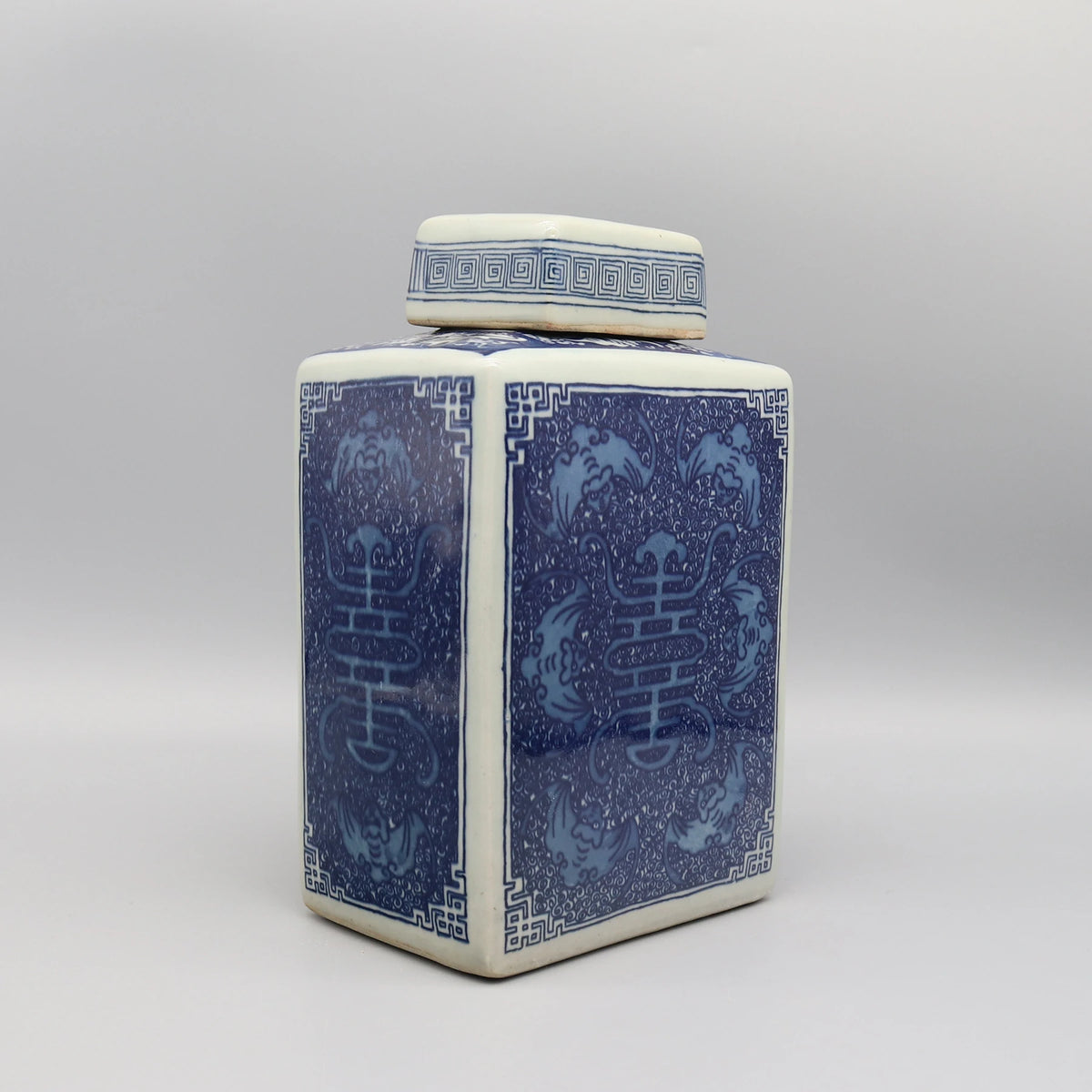 Vase en céramique de style asiatique avec motifs floraux et géométriques bleus et blancs sur un fond gris uni.