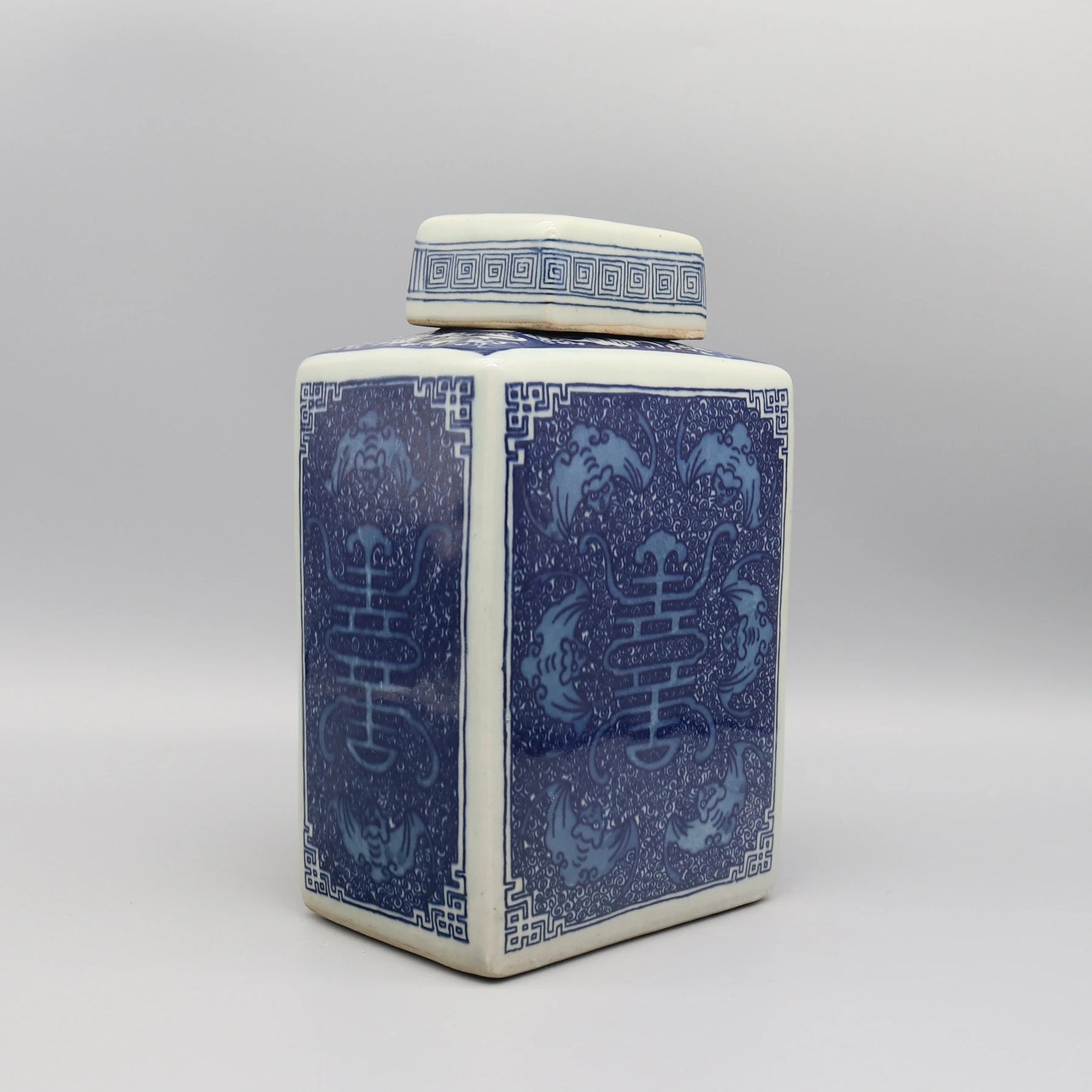 Vase en céramique de style asiatique avec motifs floraux et géométriques bleus et blancs sur un fond gris uni.