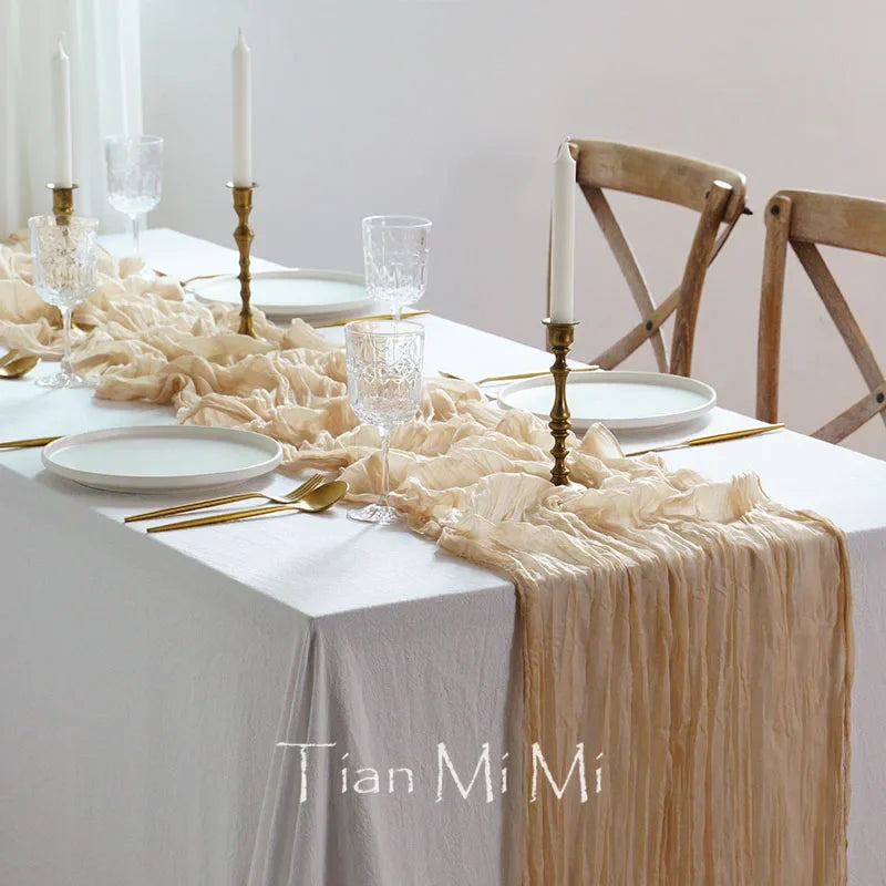 Cette image montre une table de salle à manger élégamment décorée avec de la vaisselle, des verres, des bougeoirs et une nappe de table froissée.