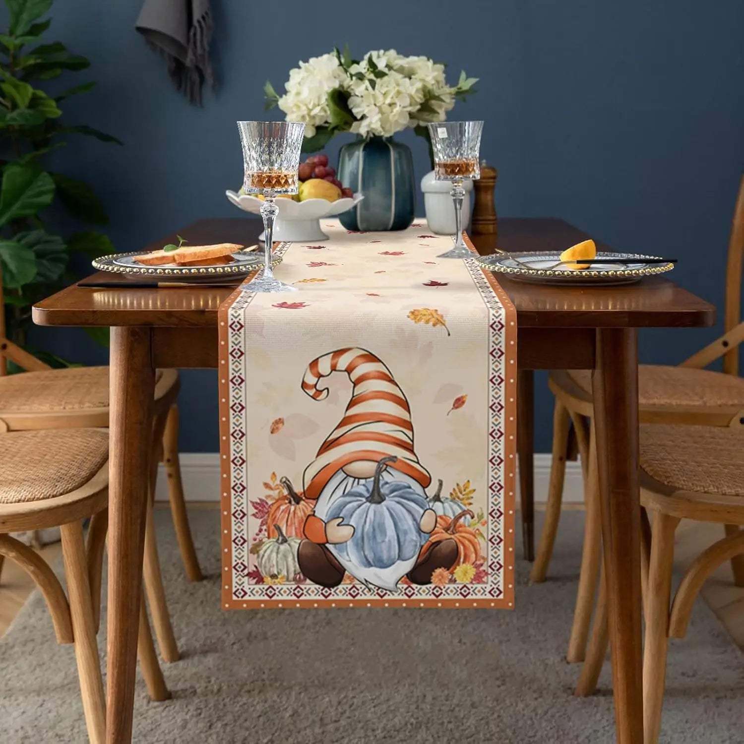 Une table élégante décorée de verres, de fruits et d'un bouquet de fleurs blanches, avec un chemin de table orné de motifs saisonniers.