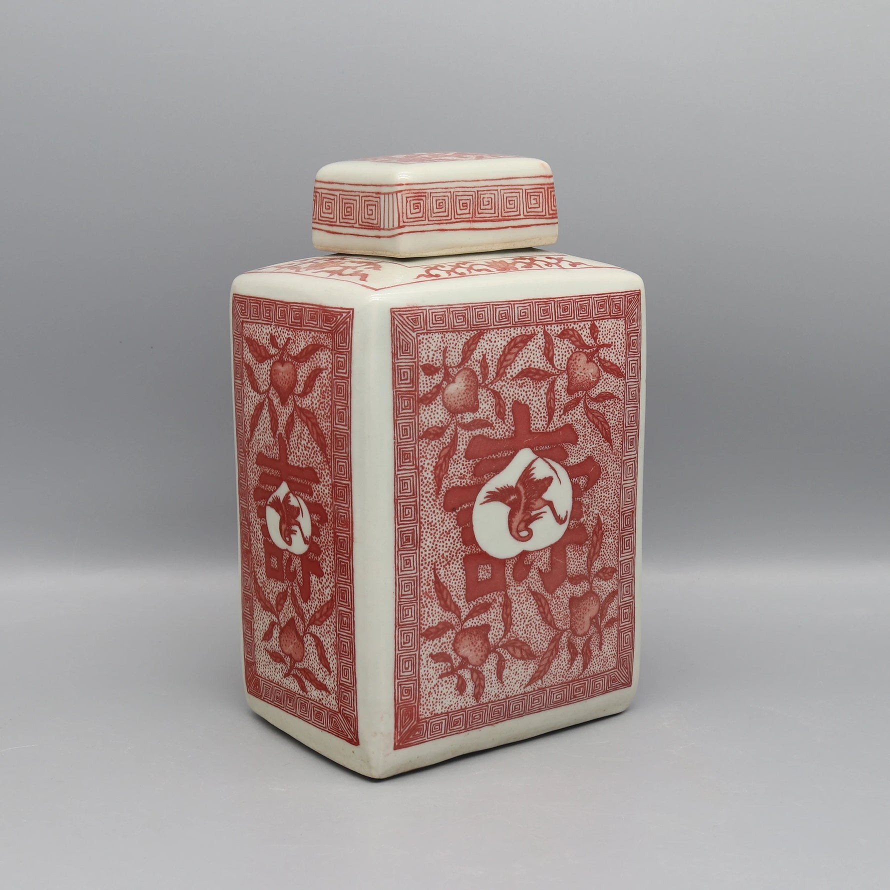 Pot décoratif en céramique blanche avec motifs floraux rouges et géométriques.