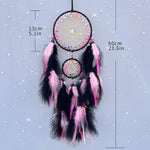 Le rêve attrapeur en forme de cercle, avec des plumes roses et noires, décoré d'éléments brillants et suspendu sur un fond étoilé.