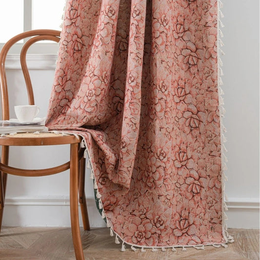Rideau fleuri vintage avec pompons, en tissu jacquard rose et beige, tombant élégamment sur une chaise en bois dans un intérieur au style rétro et naturel.