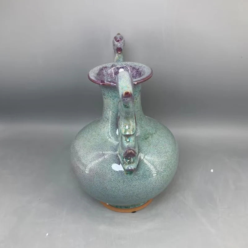 Ce vase décoratif en céramique de couleur vert pastel est orné de détails en relief et de touches de violet, créant un effet pailleté et irisé qui lui confère un aspect unique et artistique.