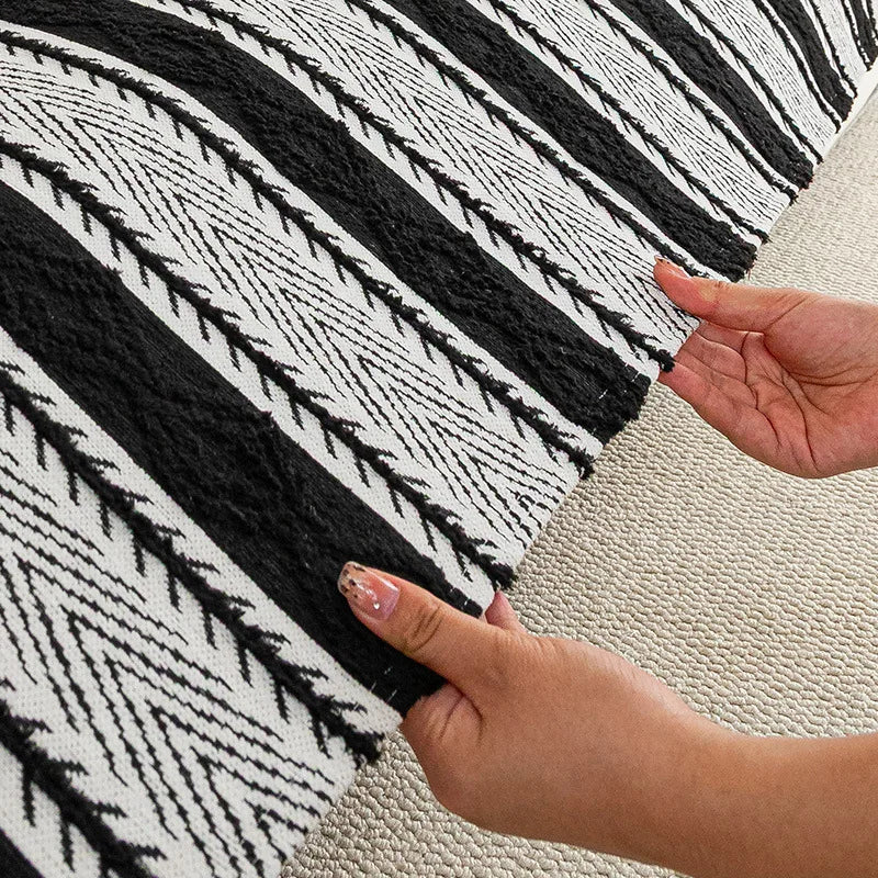 L'image montre un motif noir et blanc complexe et géométrique sur un tapis ou un tissu, avec des mains féminine sur le côté pour apprécier la texture et les couleurs.